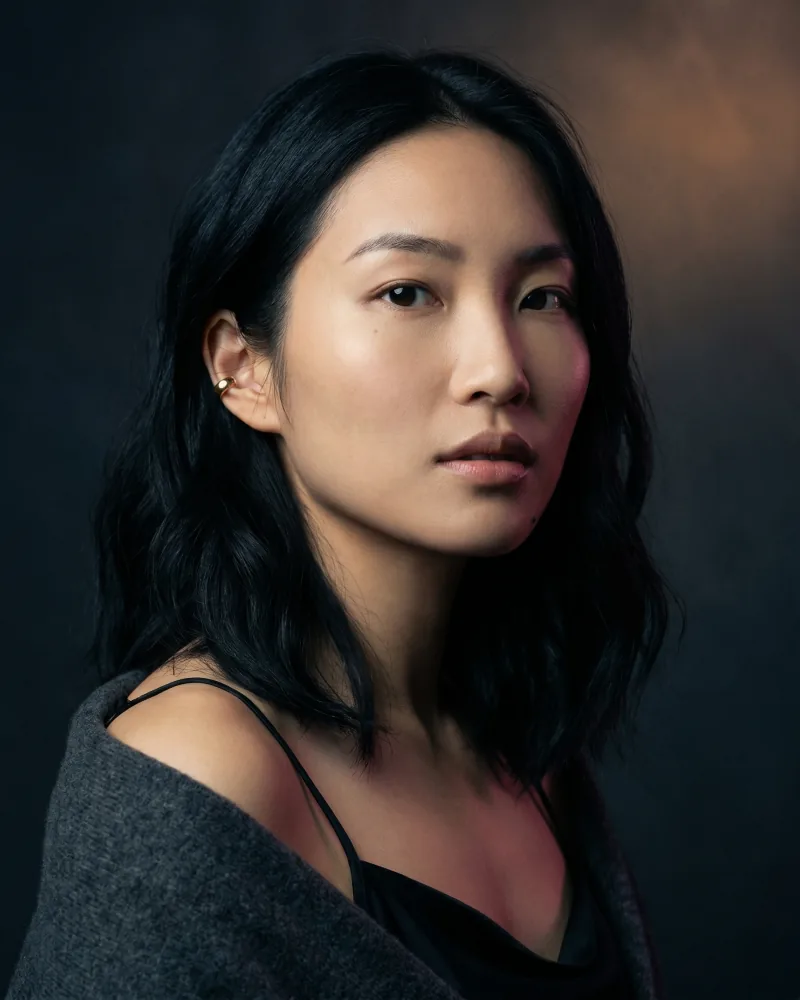 Editorial hero portrait of Mira, a Toronto creative-director archetype with dark wavy hair and gold ear cuff, against deep slate-charcoal velvet with theatrical key light, Playcut Actor Engine generation