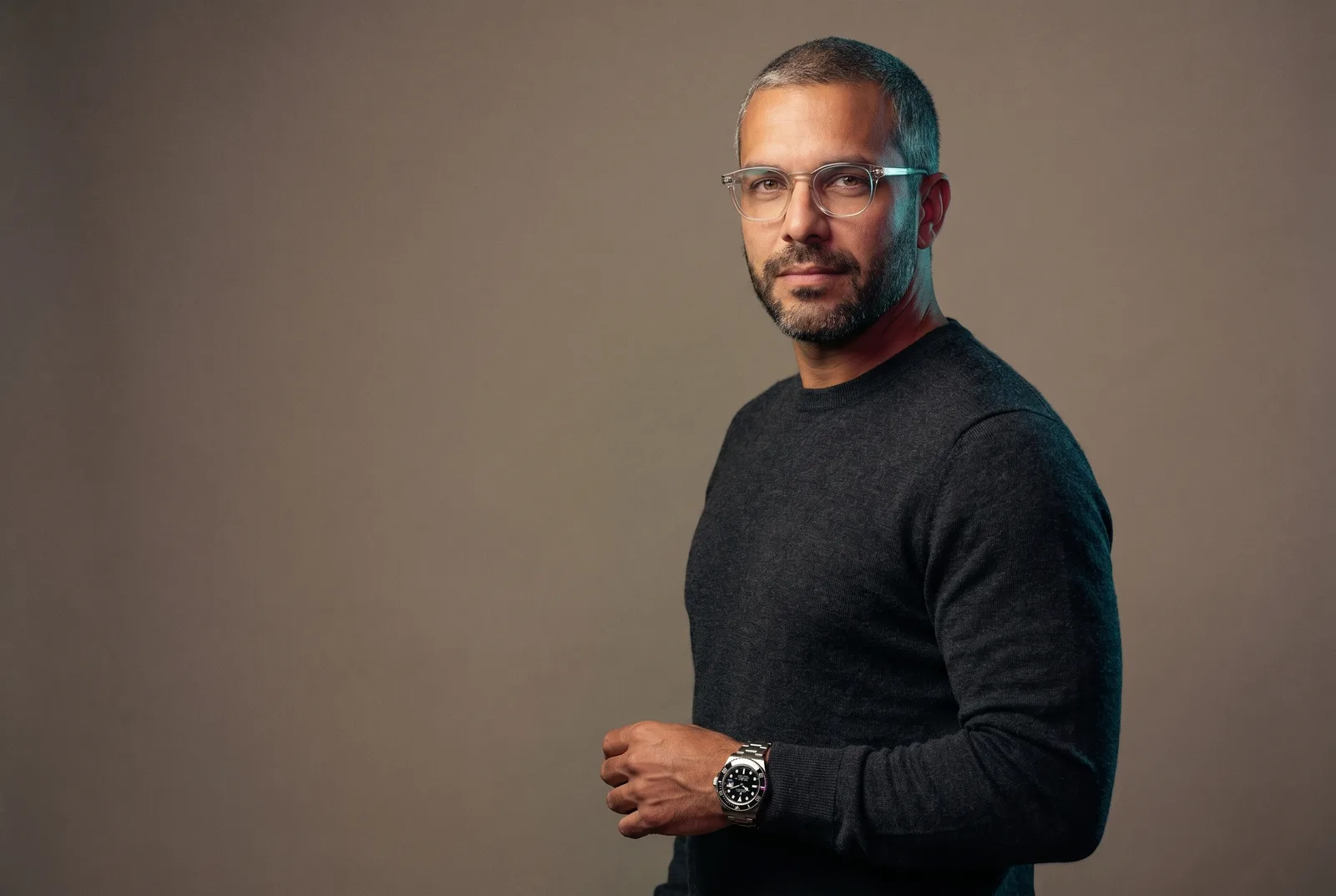 AI avatar generator showing the custom AI avatar Andre Laurent — a mid-40s spokesperson with clear-frame glasses and a steel dive watch — presenting to camera, the same avatar reused across stills, video and ads, rendered by the Playcut Actor Engine