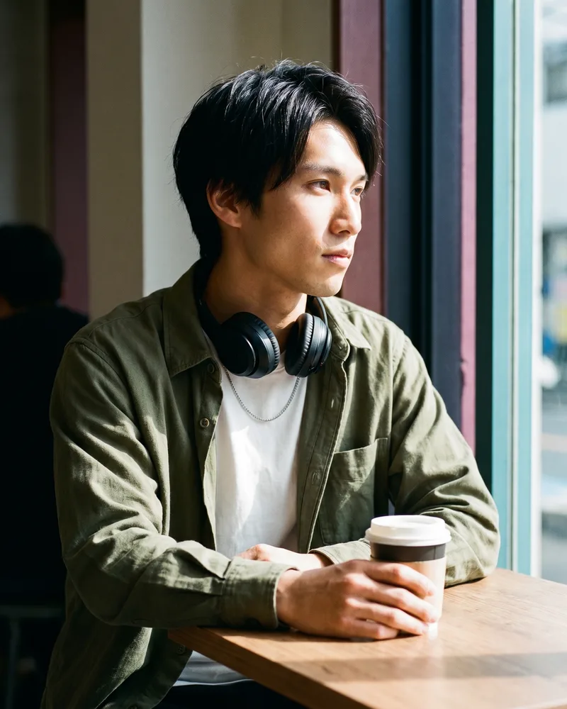 The same AI influencer persona — a young content creator with over-ear headphones and a steel chain — in a café feed-post still, the same face held across the whole feed, rendered by the Playcut Actor Engine